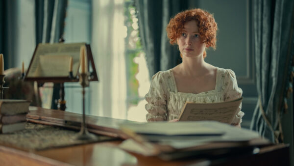 "A young woman with curly red hair in a vintage dress sits at a piano in a softly lit, elegant room with candles and sheet music, holding a music sheet and looking contemplative."
